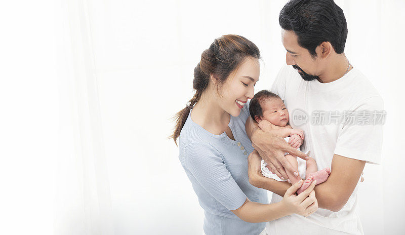 Smiling asian mother and father holding their newborn baby son at home.
